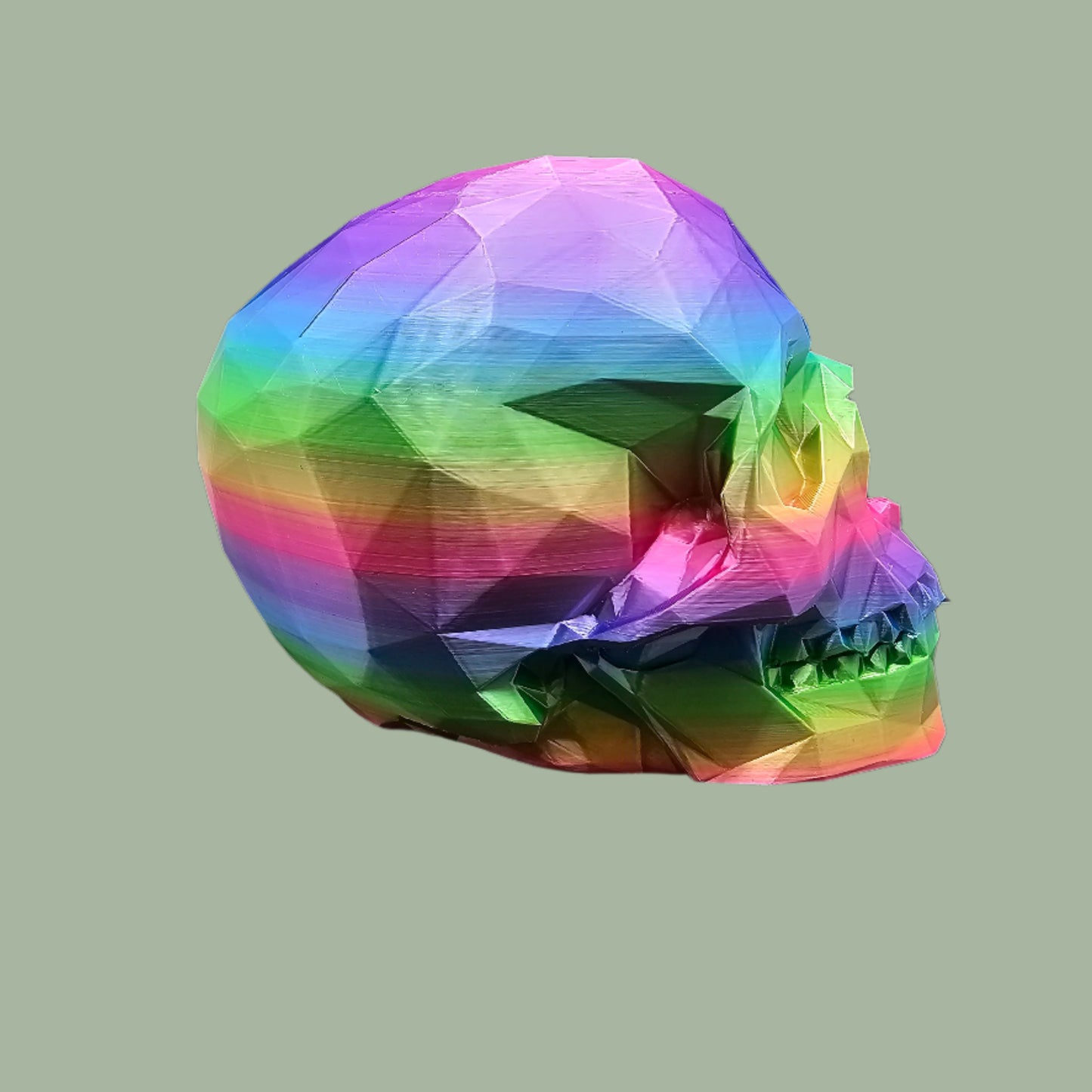 3D-printed low-poly rainbow skull figurine, uniquely coloured with a vibrant gradient. Handmade in the UK, 12cm tall, and perfect for modern home decor or gothic-inspired interiors