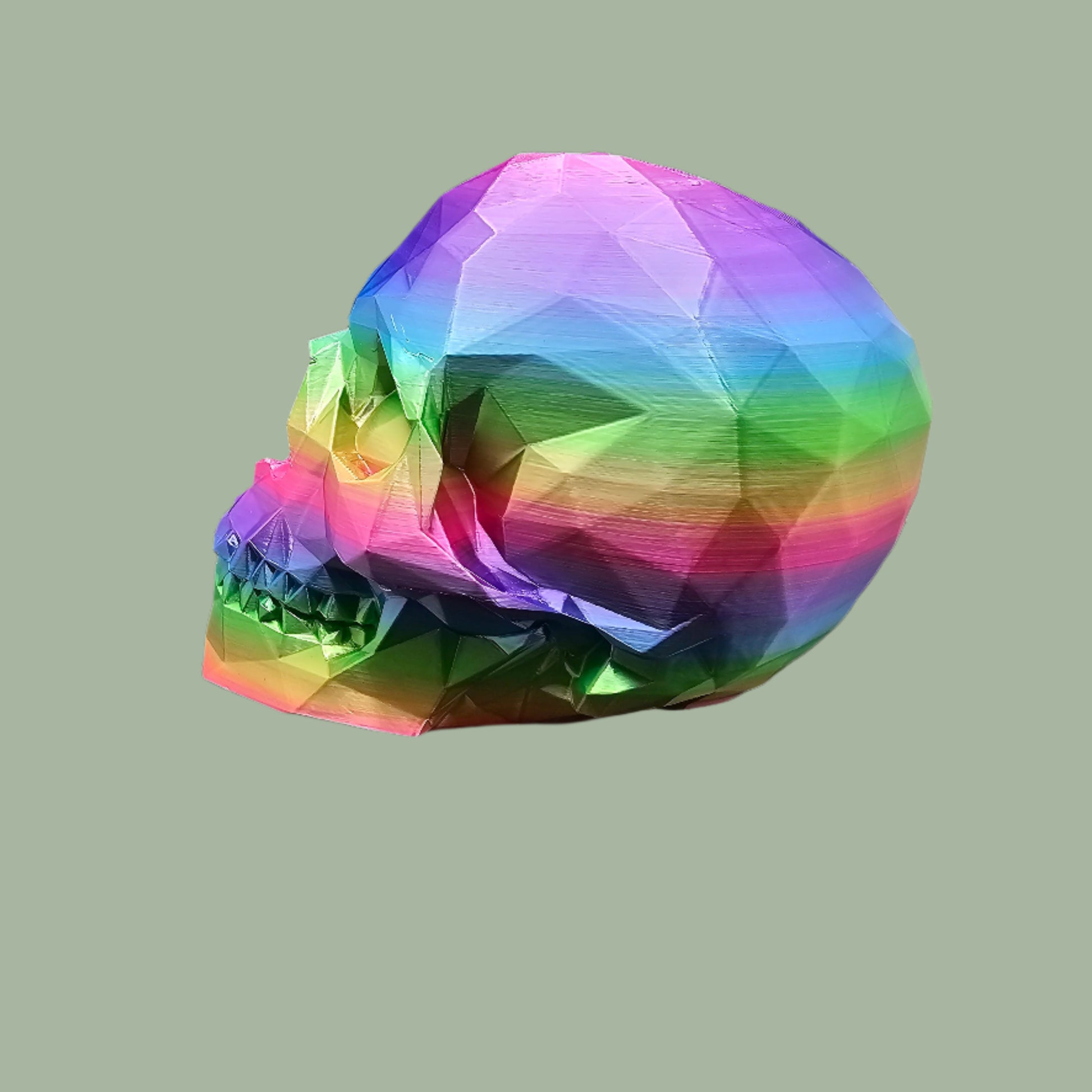 3D-printed low-poly rainbow skull figurine, uniquely coloured with a vibrant gradient. Handmade in the UK, 12cm tall, and perfect for modern home decor or gothic-inspired interiors