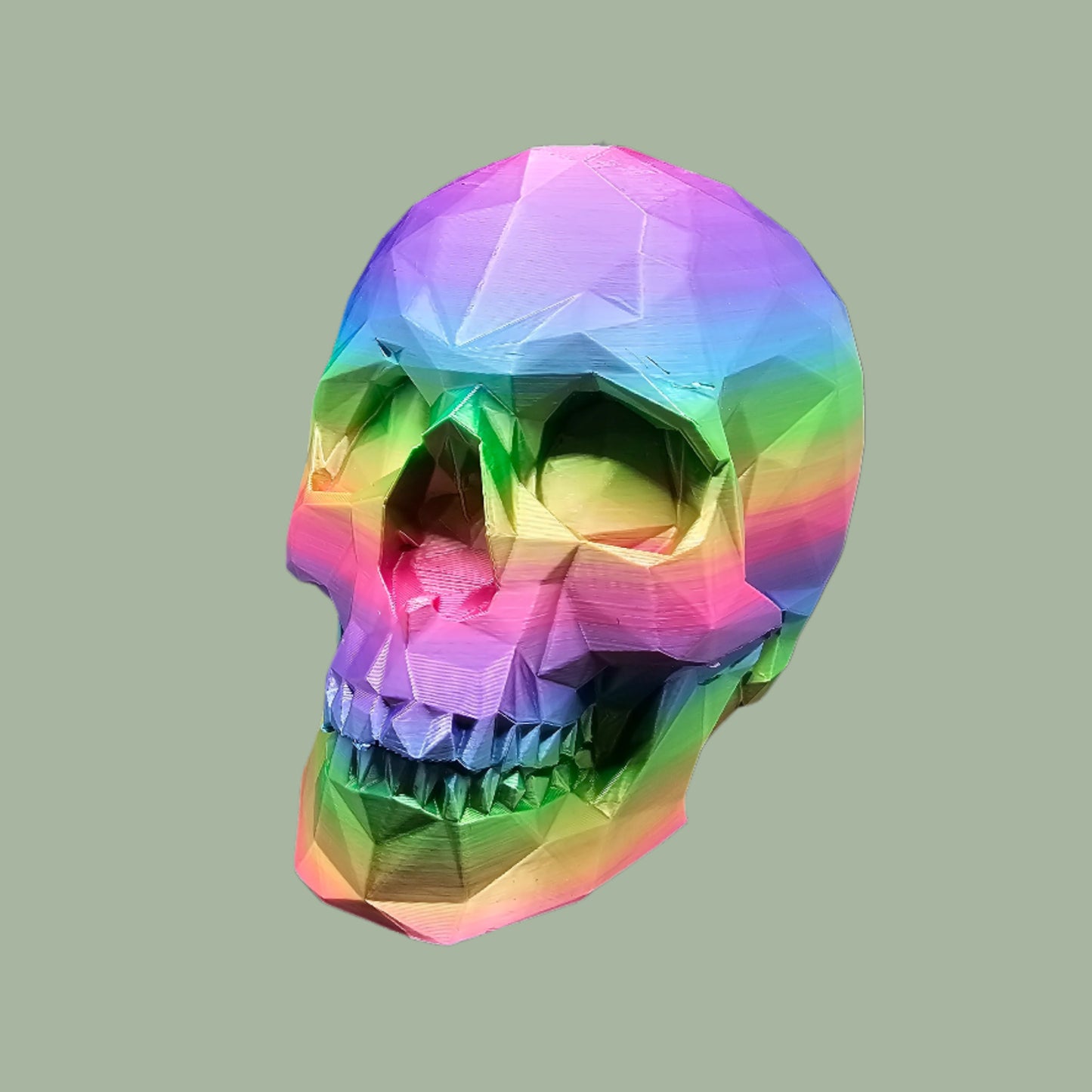 3D-printed low-poly rainbow skull figurine, uniquely coloured with a vibrant gradient. Handmade in the UK, 12cm tall, and perfect for modern home decor or gothic-inspired interiors