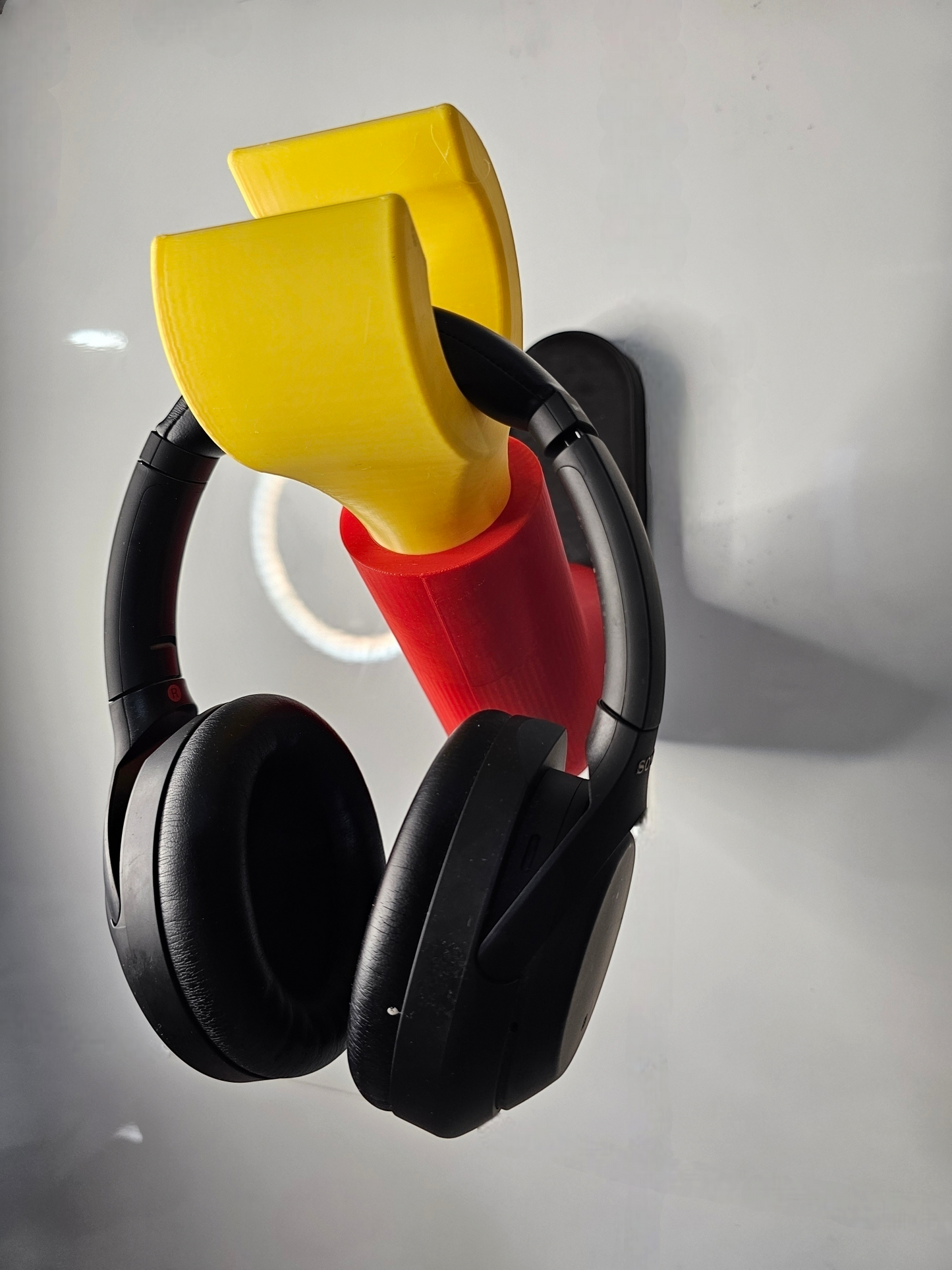 3D printed block style arm in various colours, with black base for wall or freestanding mounting, with chunky yellow hand to hold headphones or coats