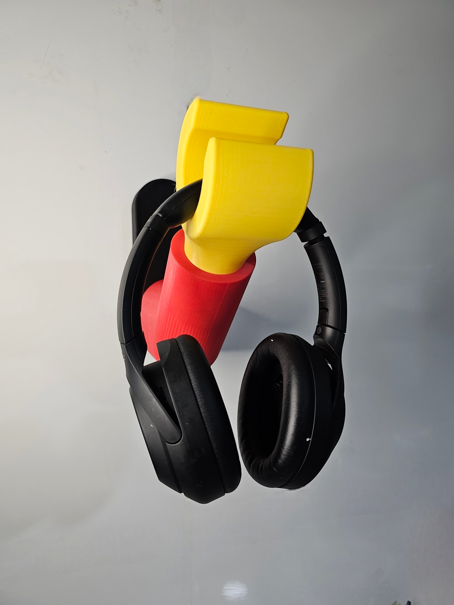 3D printed block style arm in various colours, with black base for wall or freestanding mounting, with chunky yellow hand to hold headphones or coats